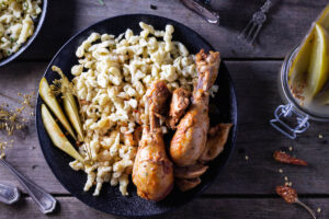 chicken drumsticks with egg noodles and pickles on a plate