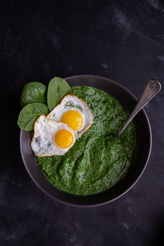 Creamed spinach and sunny side up eggs in black bowl with a vintage spoon