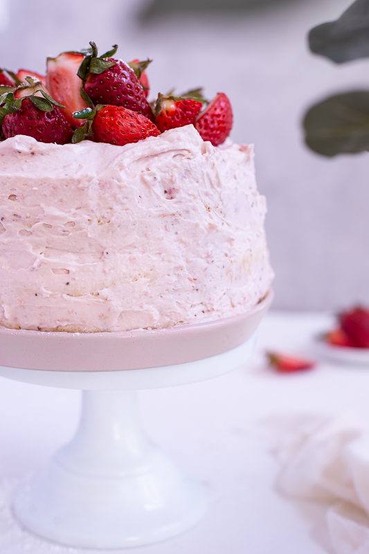 strawberry mascarpone cake on a white cake stand with cut strawberries on top